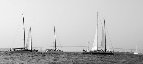 the farr 40 fleet sails by the newport bridge at sunset